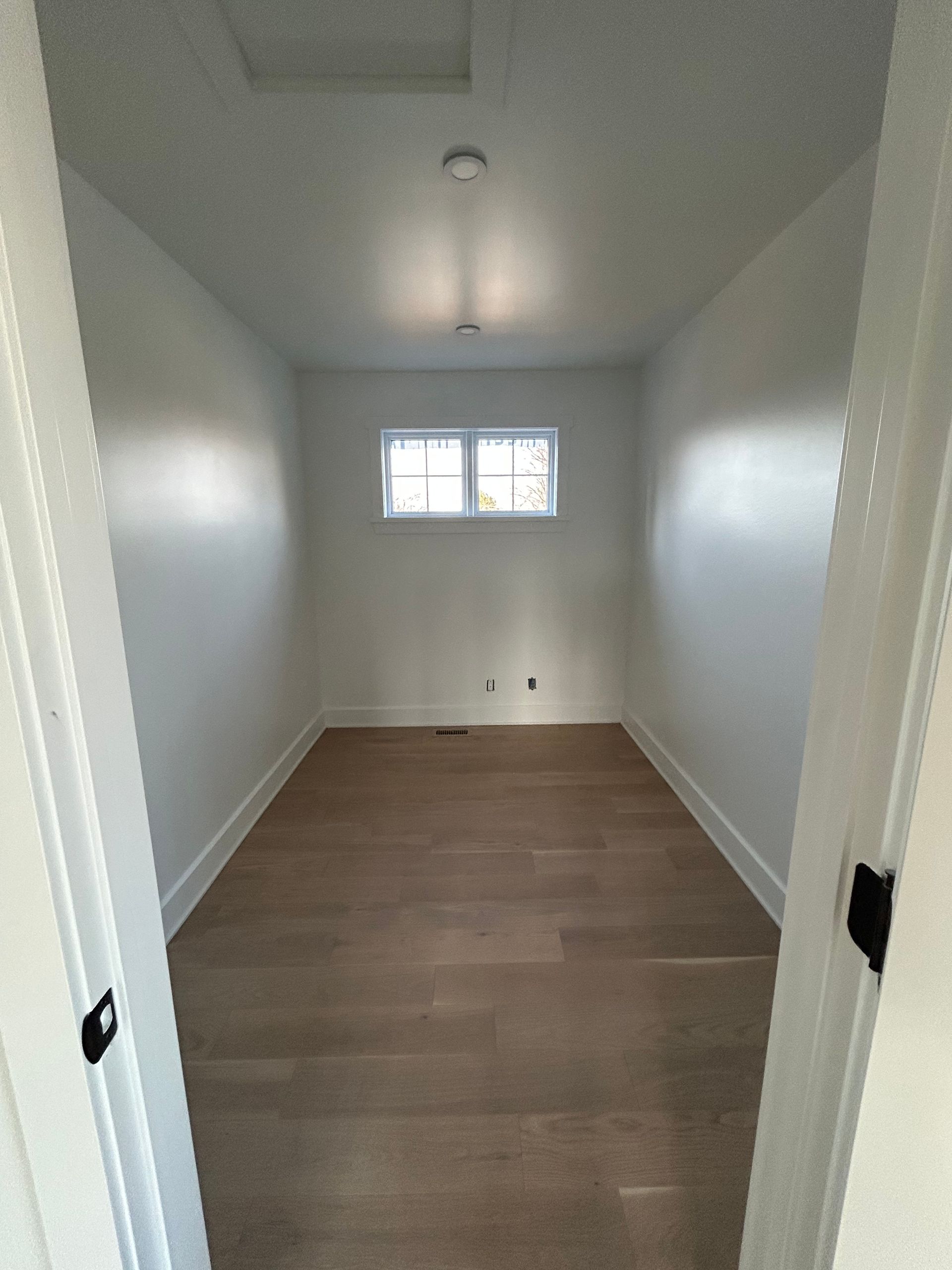 Pièce blanche vide avec parquet, petite fenêtre et plafonnier