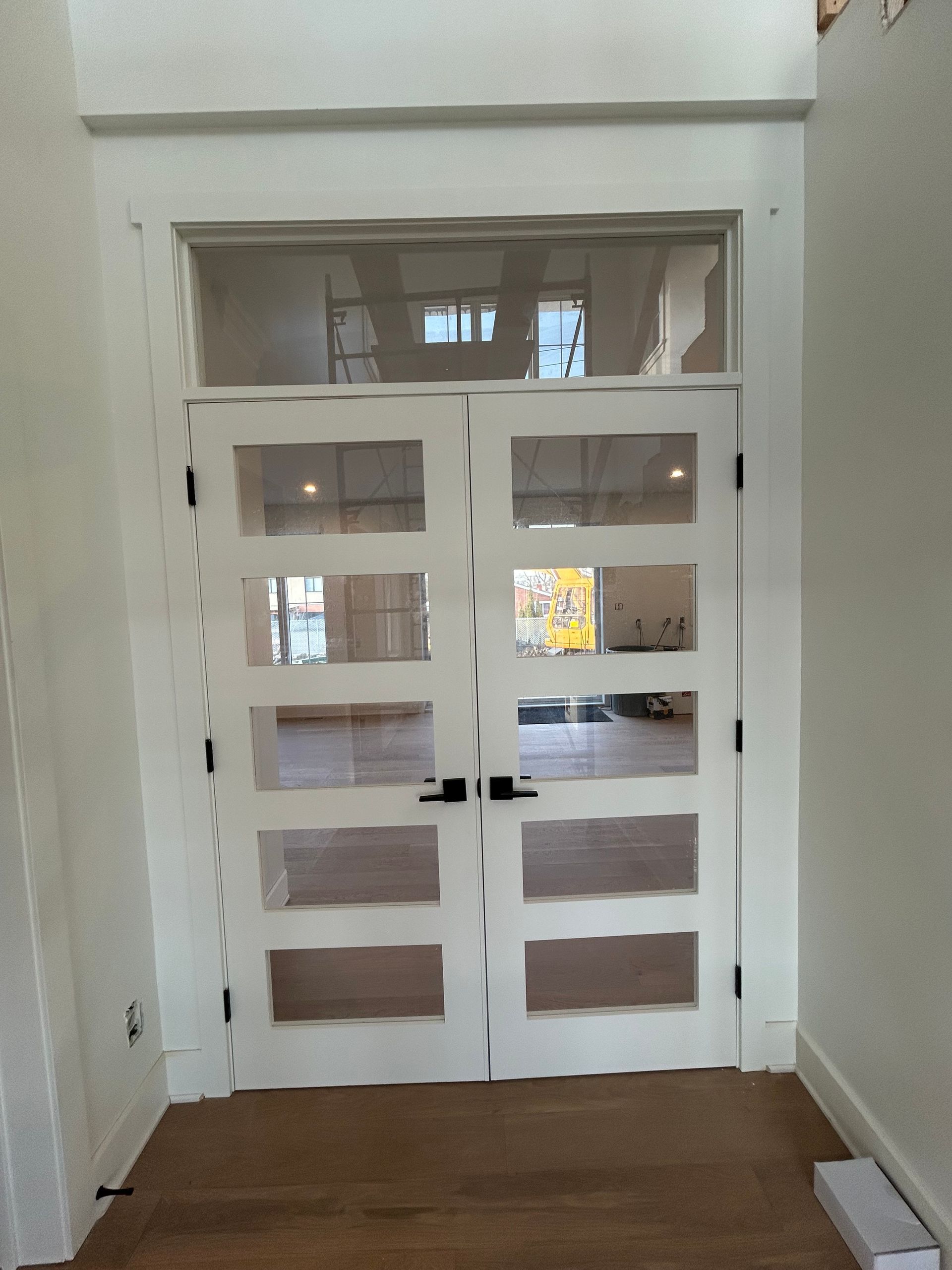 Double porte-fenêtre blanche dans un couloir, avec de petits carreaux de verre et une imposte étroite au-dessus.