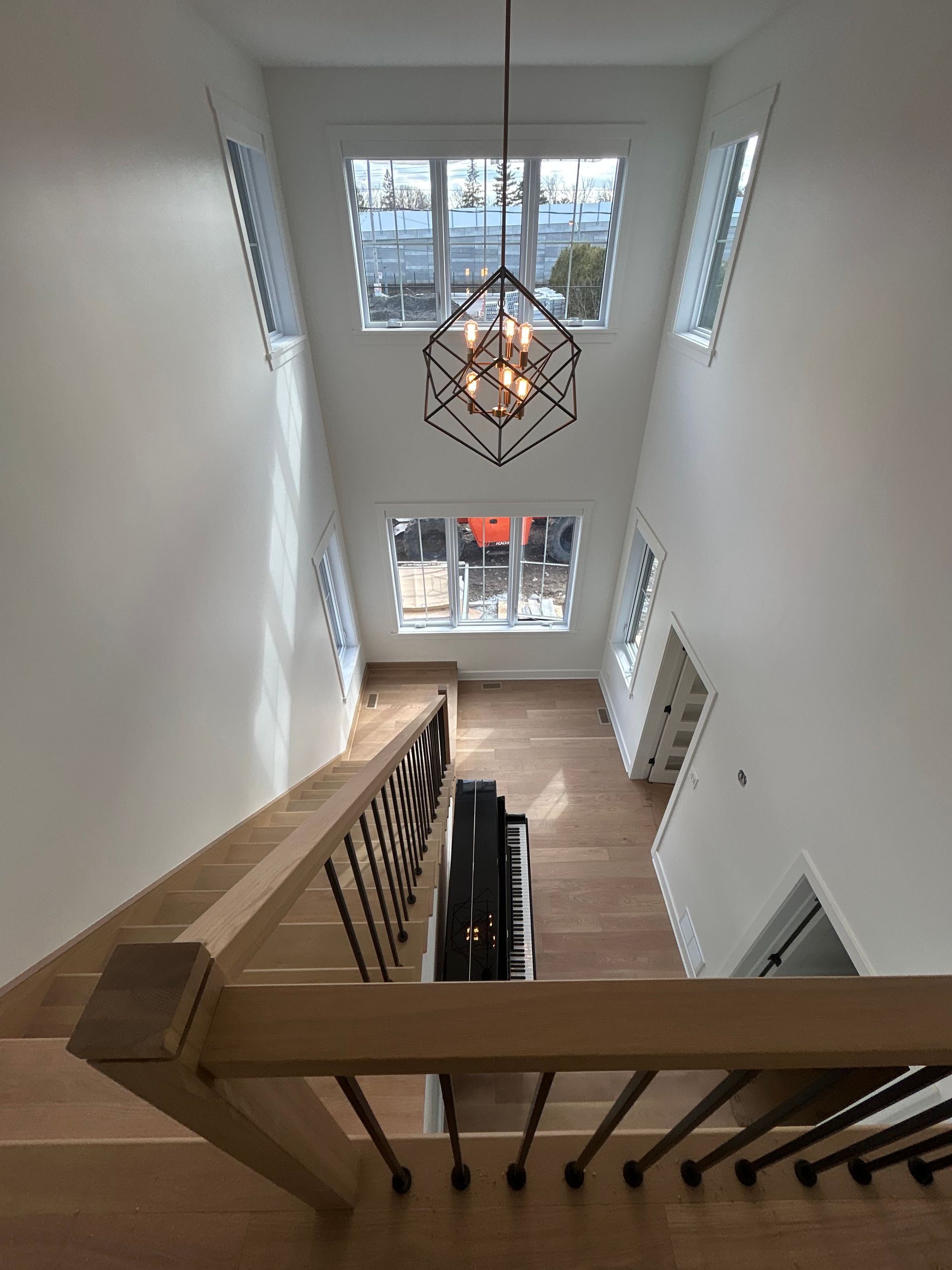 Cage d'escalier aux murs blancs, rampe en bois, suspension lumineuse géométrique et lumière naturelle provenant des fenêtres du dessous
