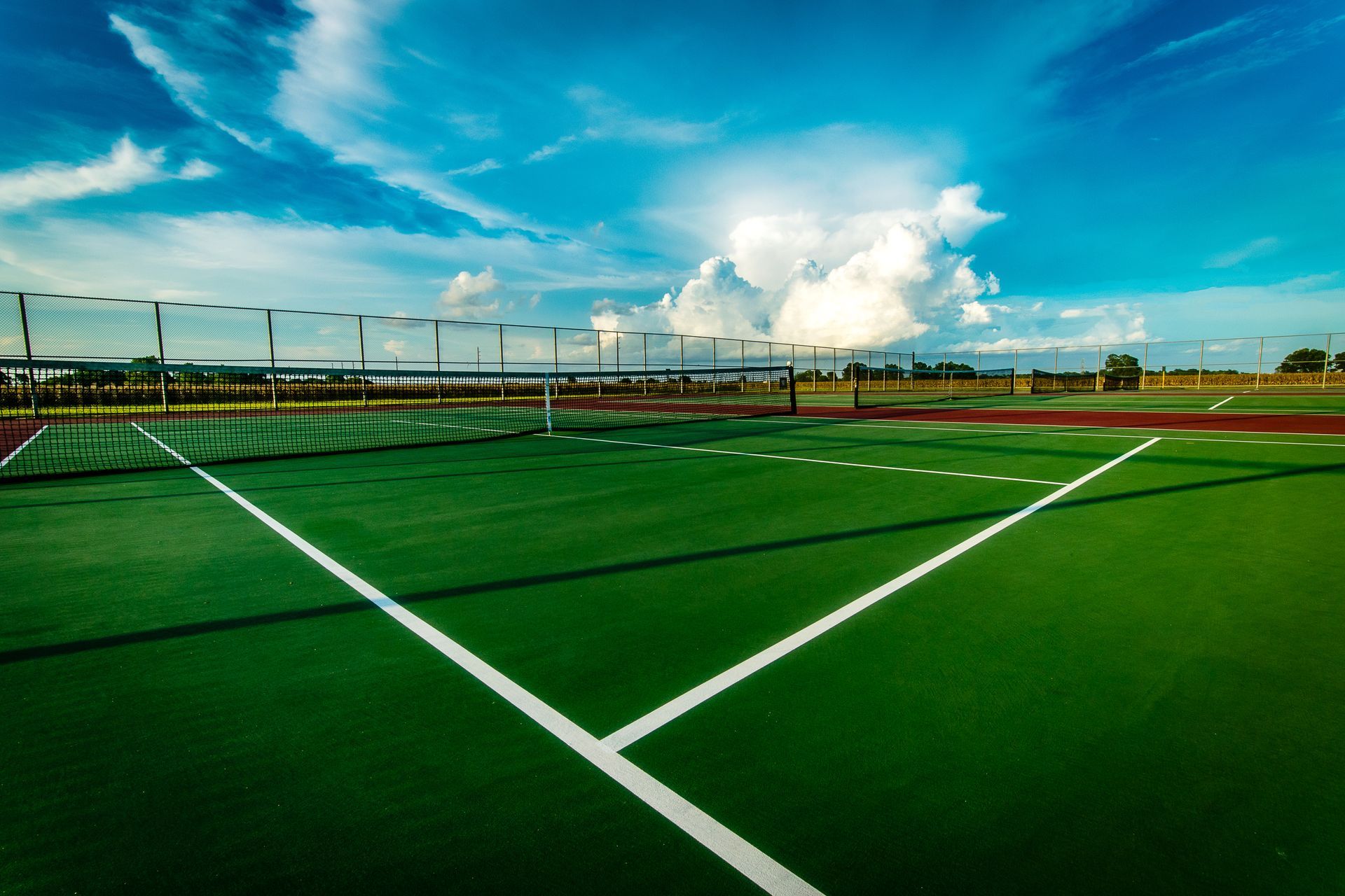 Empty outdoor sports court with green turf, white lines, and a blue sky with clouds