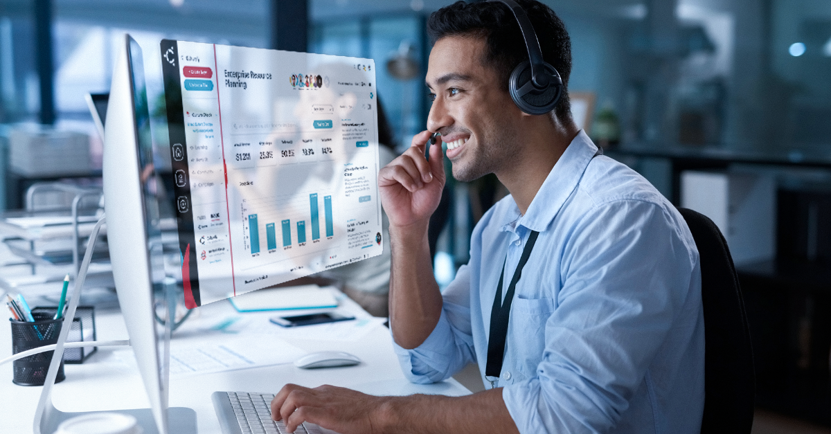 A man wearing headphones is talking on a cell phone while sitting in front of a computer.