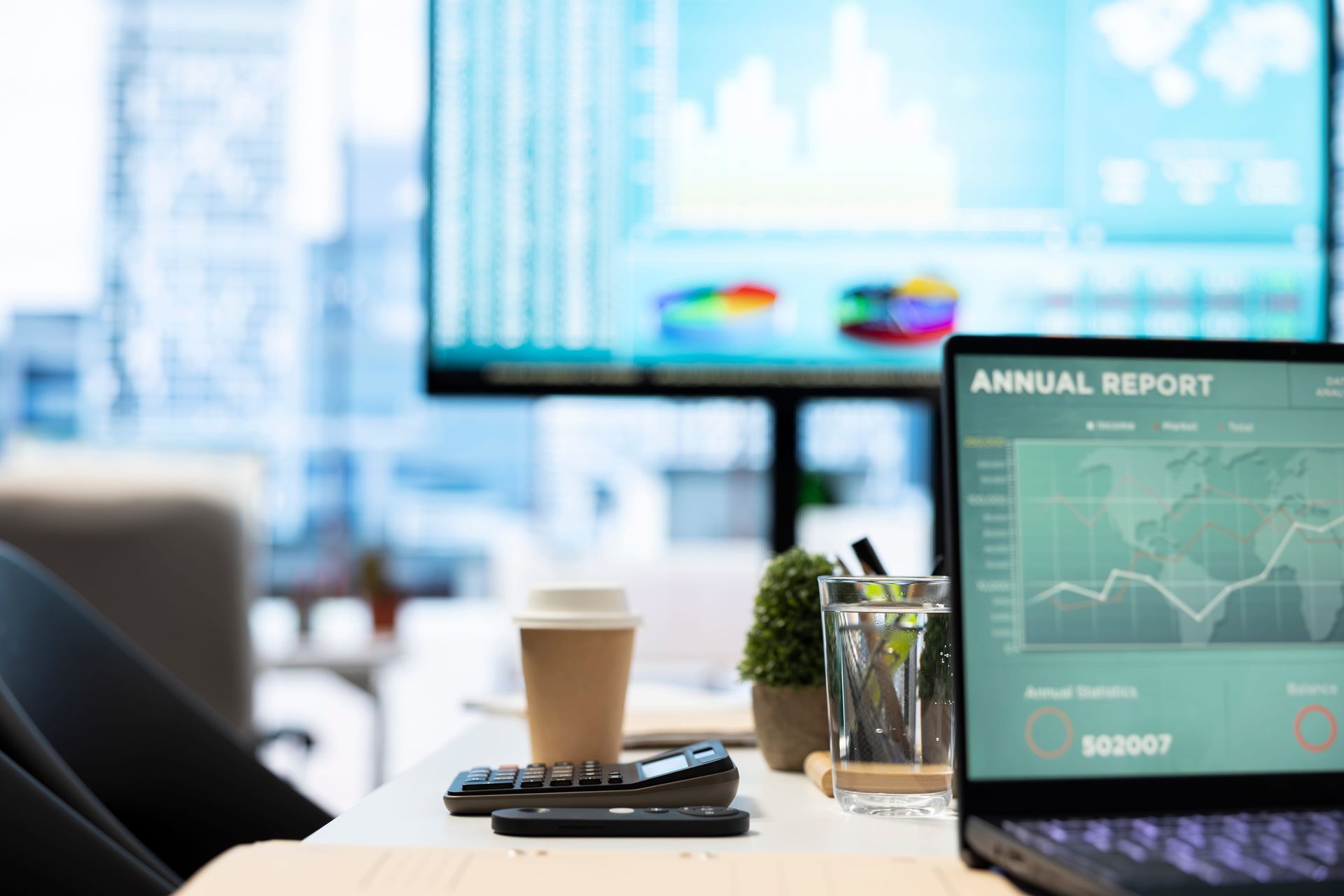 Office desk with laptop showing annual report, coffee cup, and city view through bright windows
