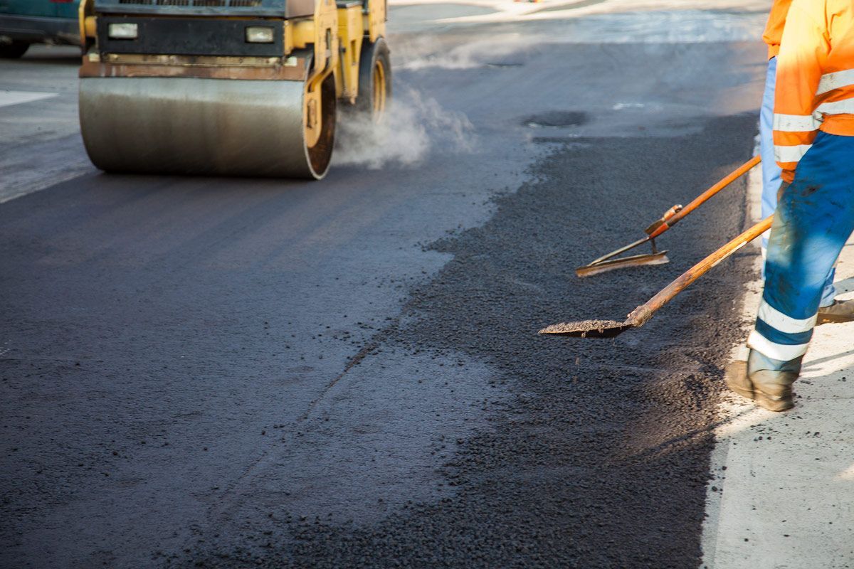 A Man Standing Next to A Roller on A Road — Omaha, NE — Omaha Paving Company