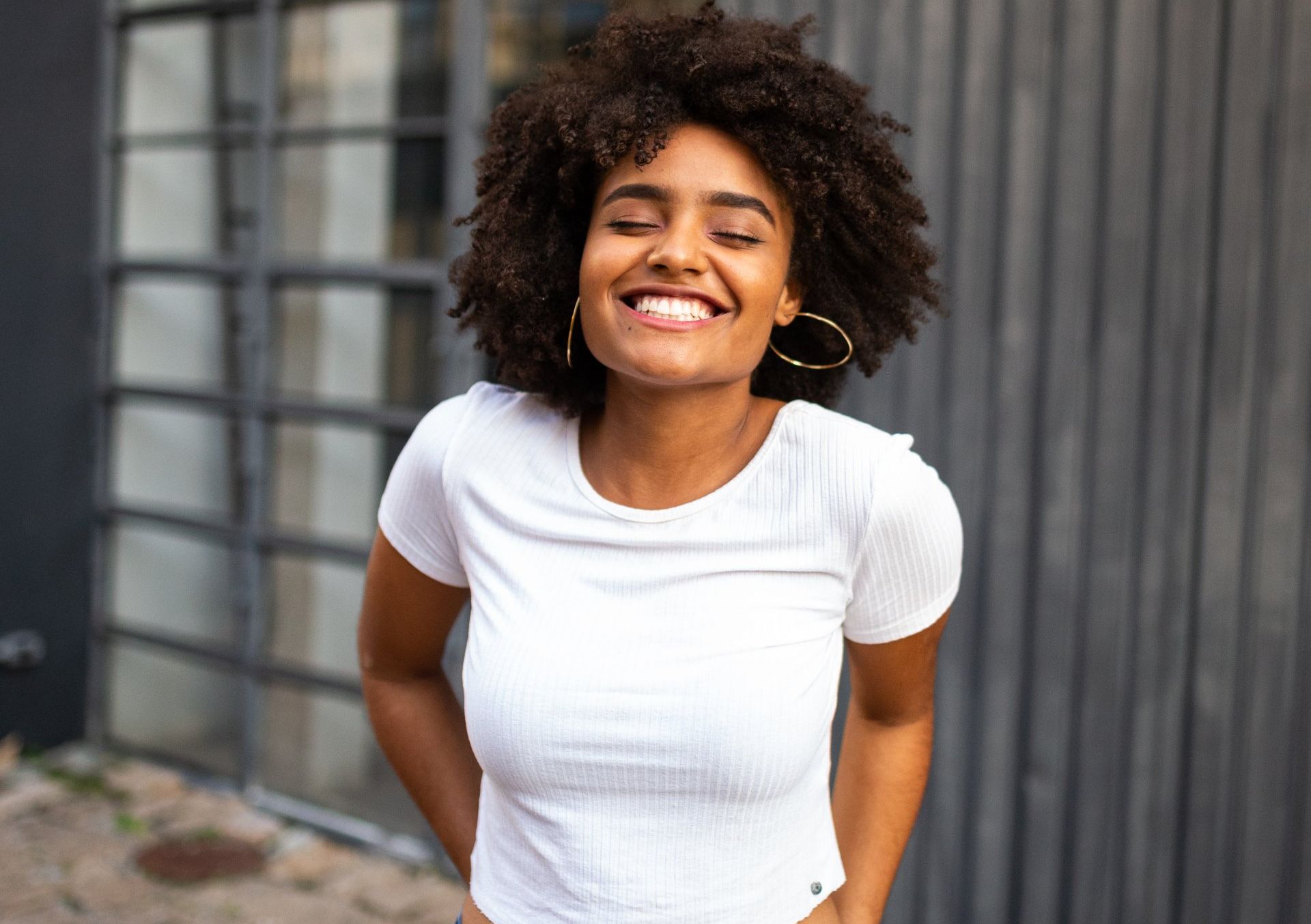 A woman in a white shirt is smiling with her eyes closed.