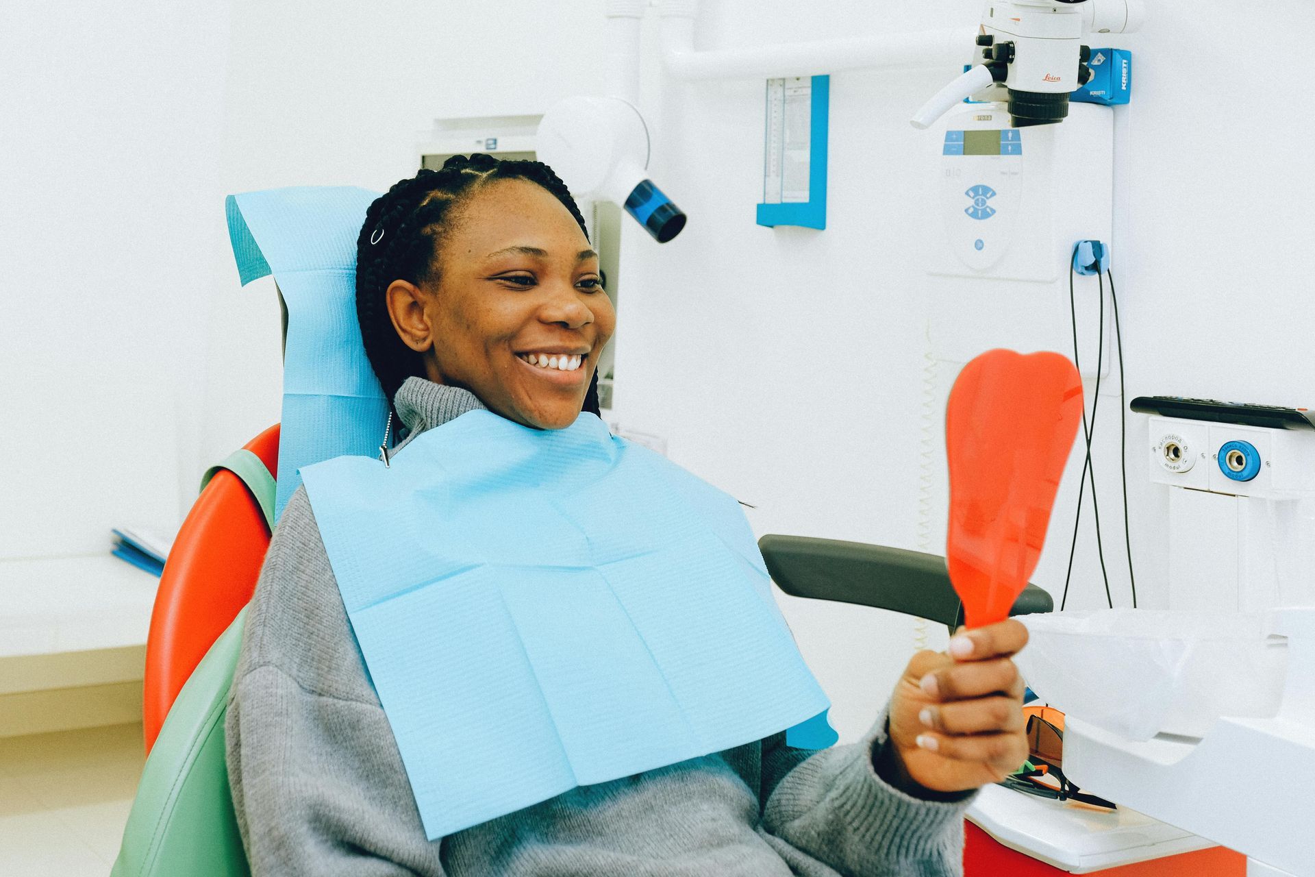 Woman smiles in a dentist chair, looking at a handheld mirror, checking her teeth.