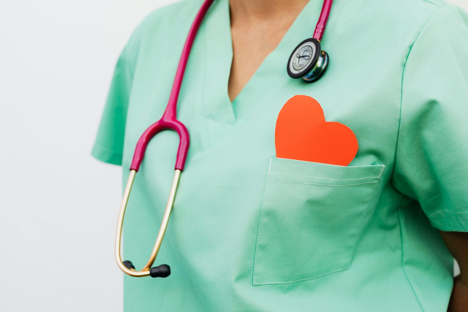 Doctor wearing green scrubs with a stethoscope and a red heart in their pocket.