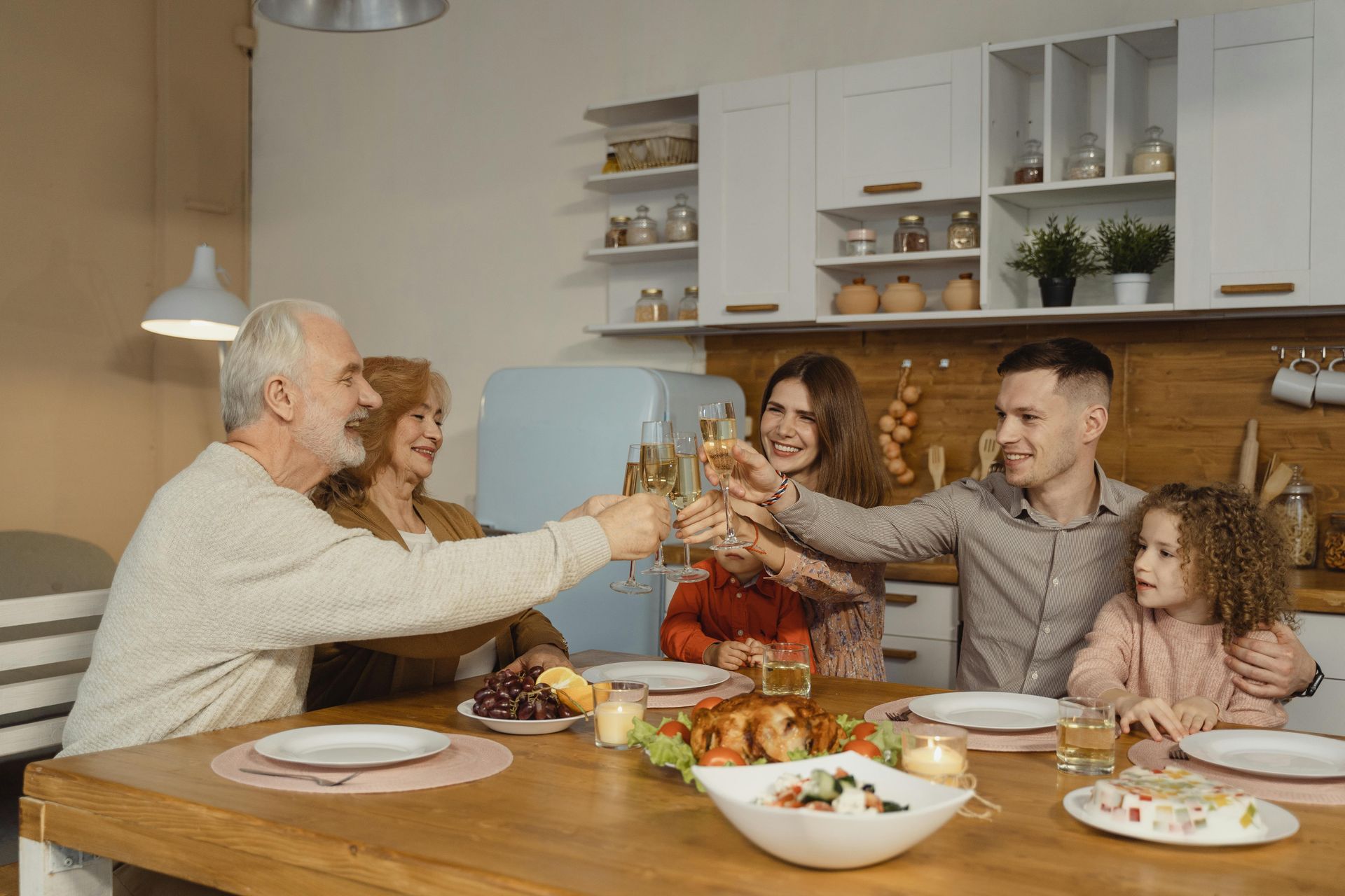 Family toasting with champagne at a dining table in a kitchen, smiling.