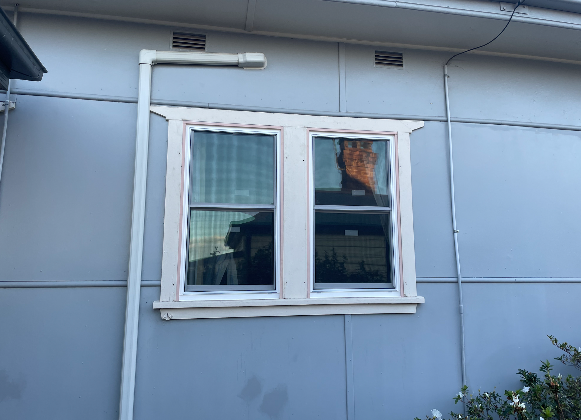 White-framed window on a blue exterior wall with a small vent above it.