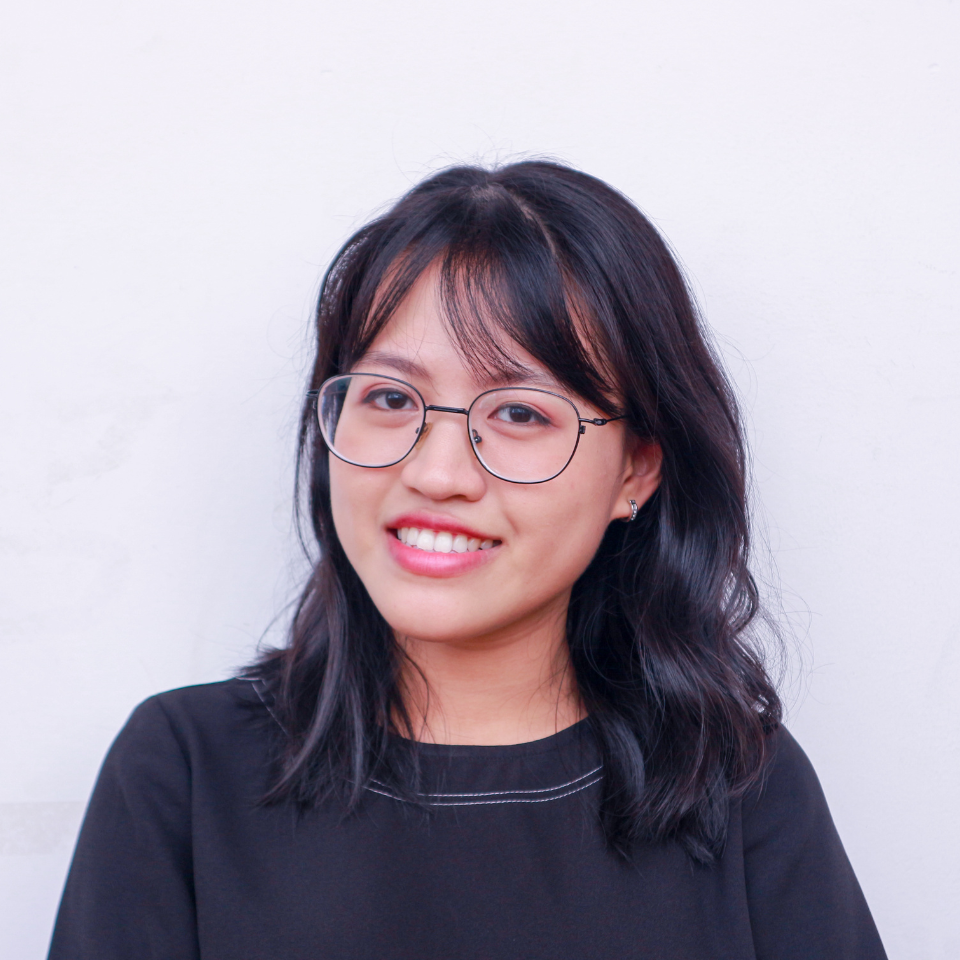 Woman with black hair and glasses smiles at the camera, wearing a black shirt against a white background.