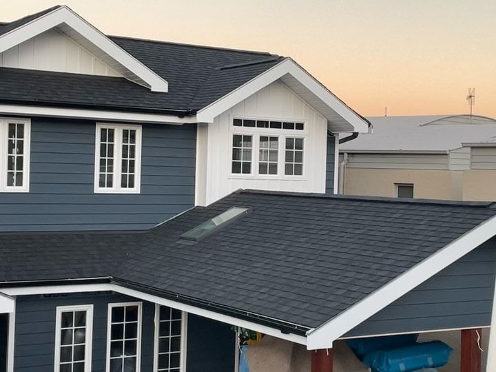 Two-story house with dark blue siding and a black shingle roof. White trim surrounds the windows and roof edges.