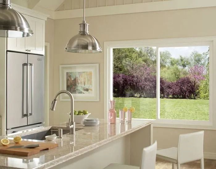 Kitchen with a stainless steel refrigerator, island with a sink, and a window overlooking a green lawn and blooming trees.