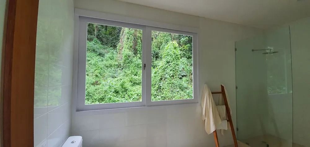 A bathroom with a large window overlooking lush green foliage. A towel hangs on a wooden ladder.