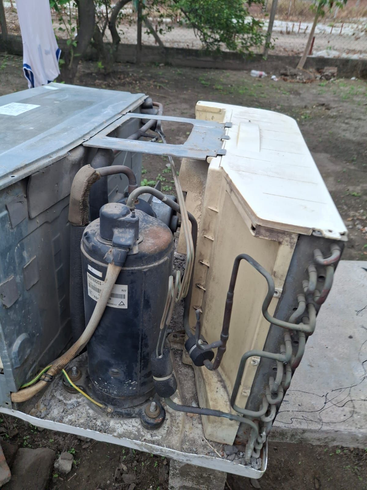 Unidad exterior de climatización con compresor expuesto y tuberías de refrigerante en espiral sobre una base de hormigón.