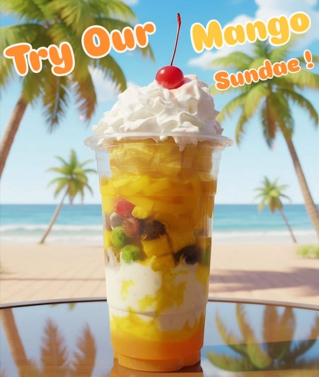 Mango sundae in a clear cup topped with whipped cream and cherry on a beachside table, with palms and ocean behind