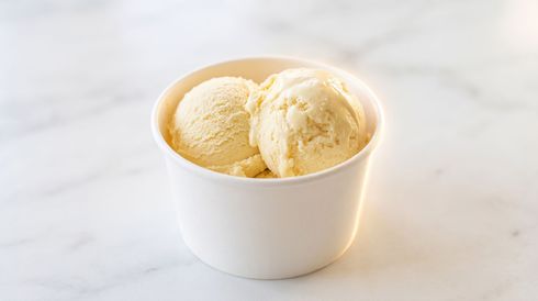 Two scoops of vanilla ice cream in a white cup on a light marble surface