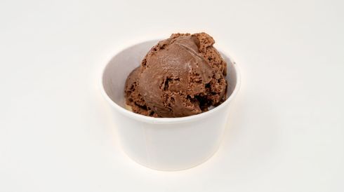 A scoop of chocolate ice cream in a small white bowl on a white background