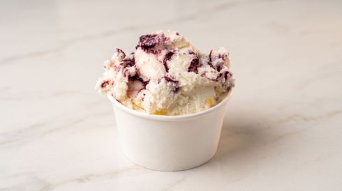 Cup of vanilla ice cream topped with berry swirls on a light marble surface