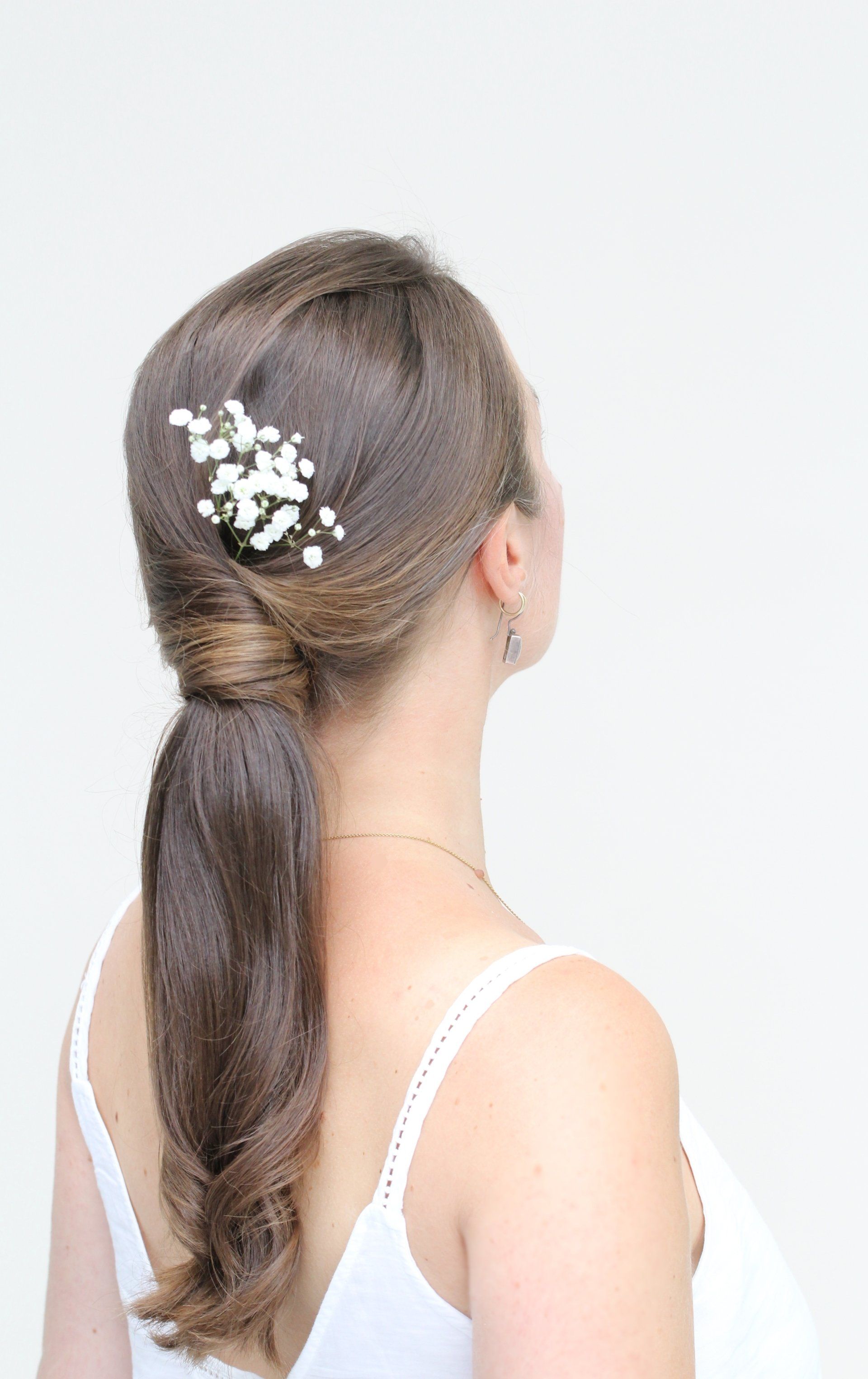 Der Rücken einer Frau, die ein weißes Tanktop und einen Pferdeschwanz mit Blumen im Haar trägt.