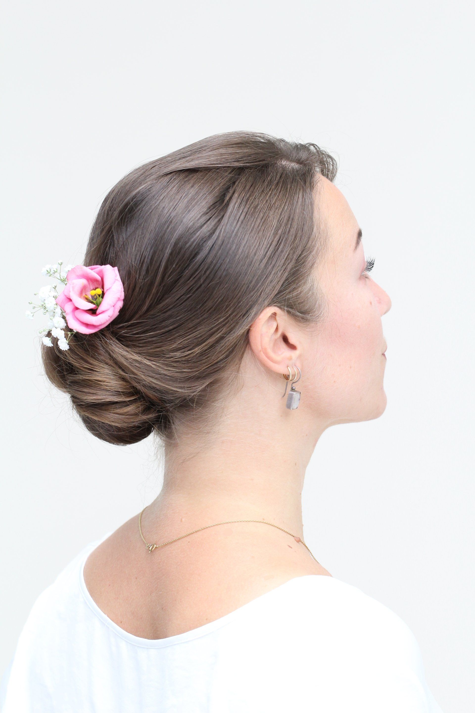 Eine Frau trägt einen Dutt mit einer rosa Blume im Haar.