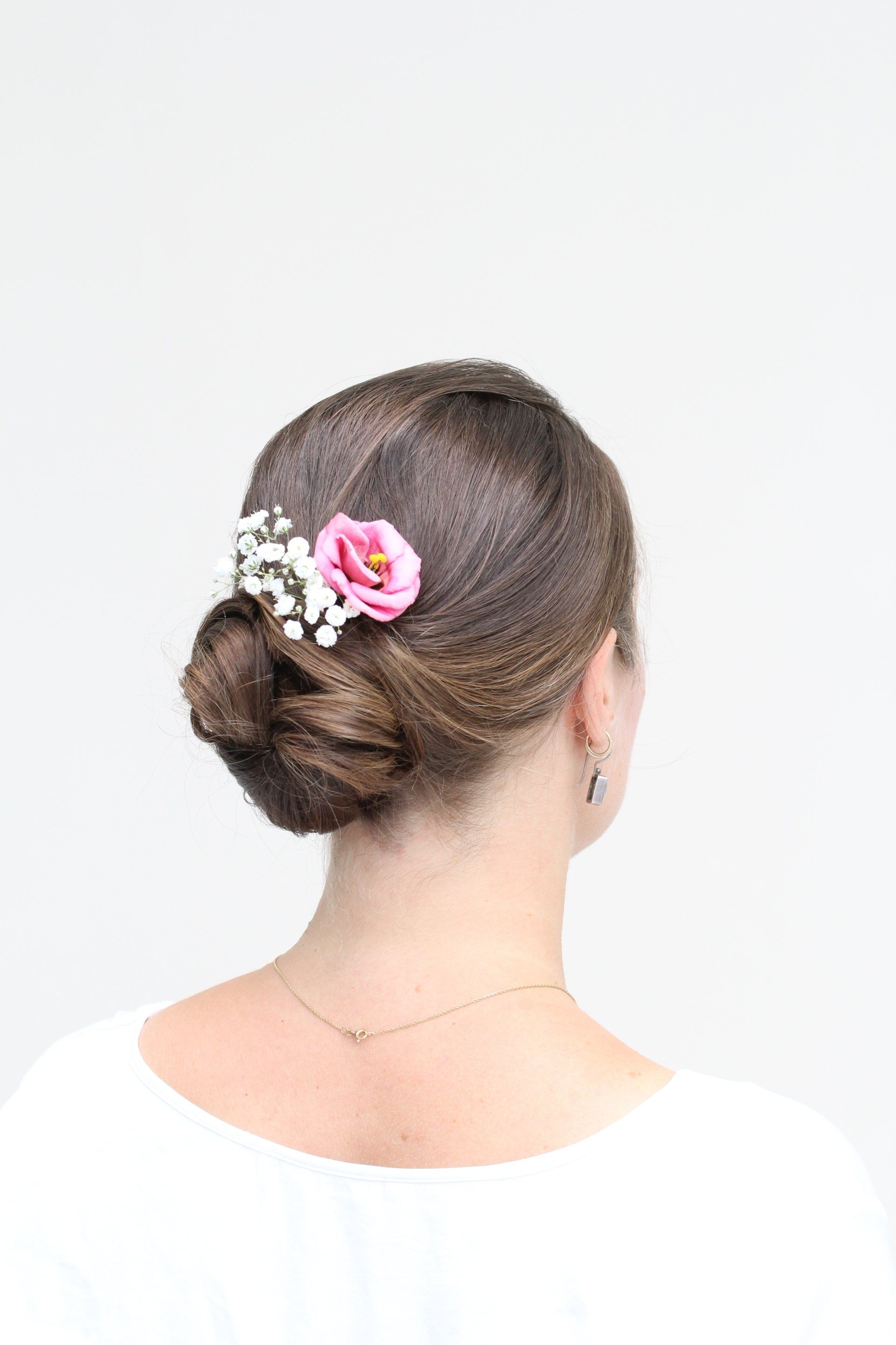Eine Frau trägt einen Dutt mit einer rosa Blume im Haar.