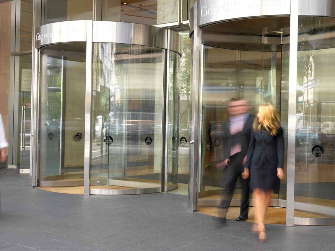 A man and a woman are walking through a revolving glass door