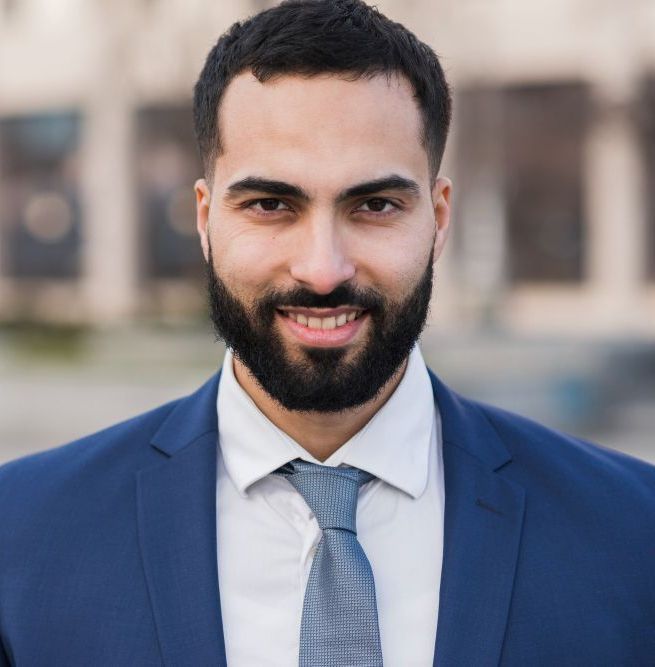 A man with a beard is wearing a blue suit and tie.