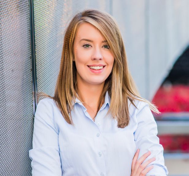 A woman is leaning against a wall with her arms crossed and smiling.
