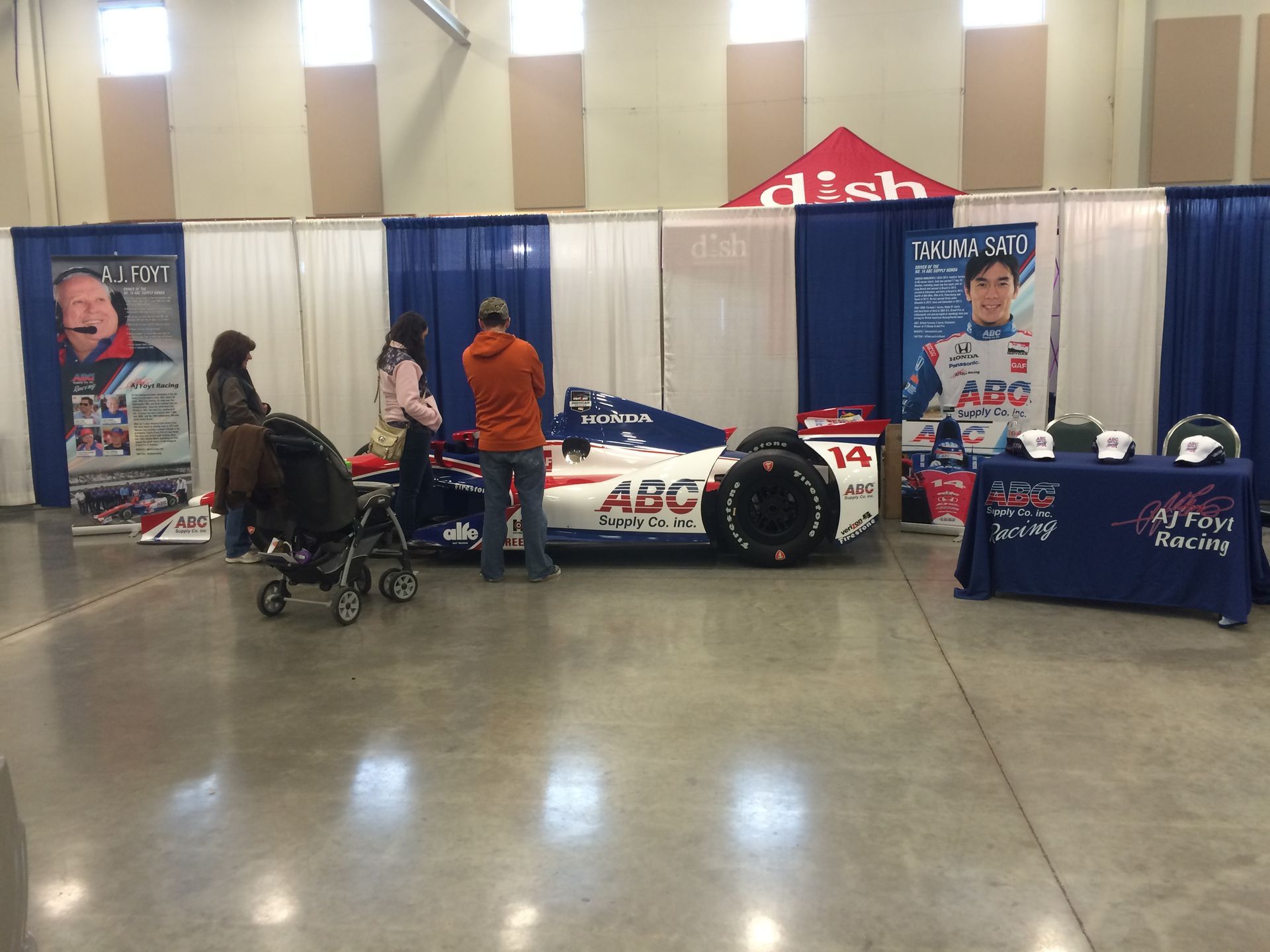A race car is on display in a room with people looking at it.
