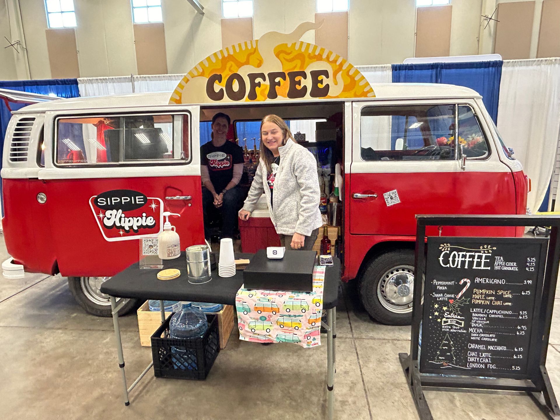 A woman is standing in front of a red coffee van.