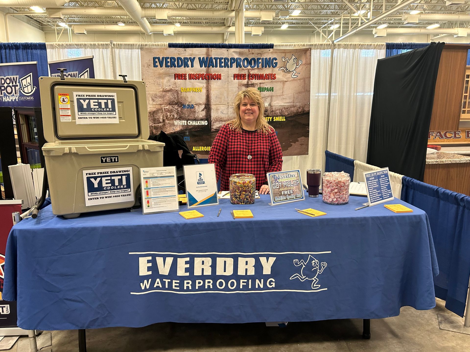 A woman is standing in front of a table with a blue table cloth that says everdry waterproofing.