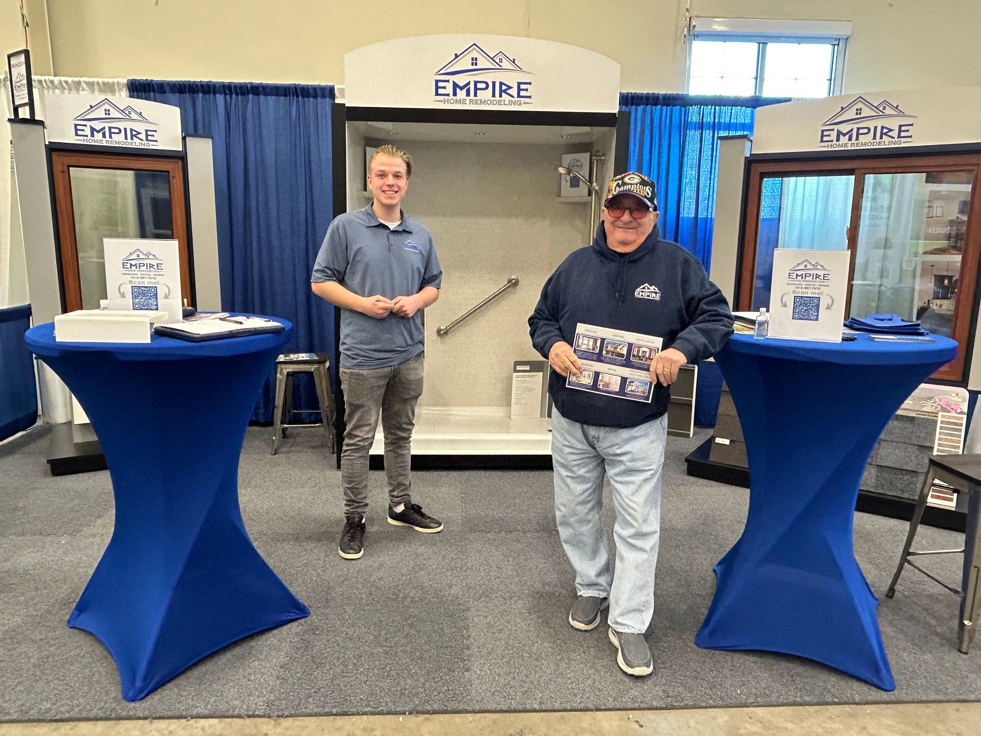 Two men are standing next to each other in a room with blue tables.