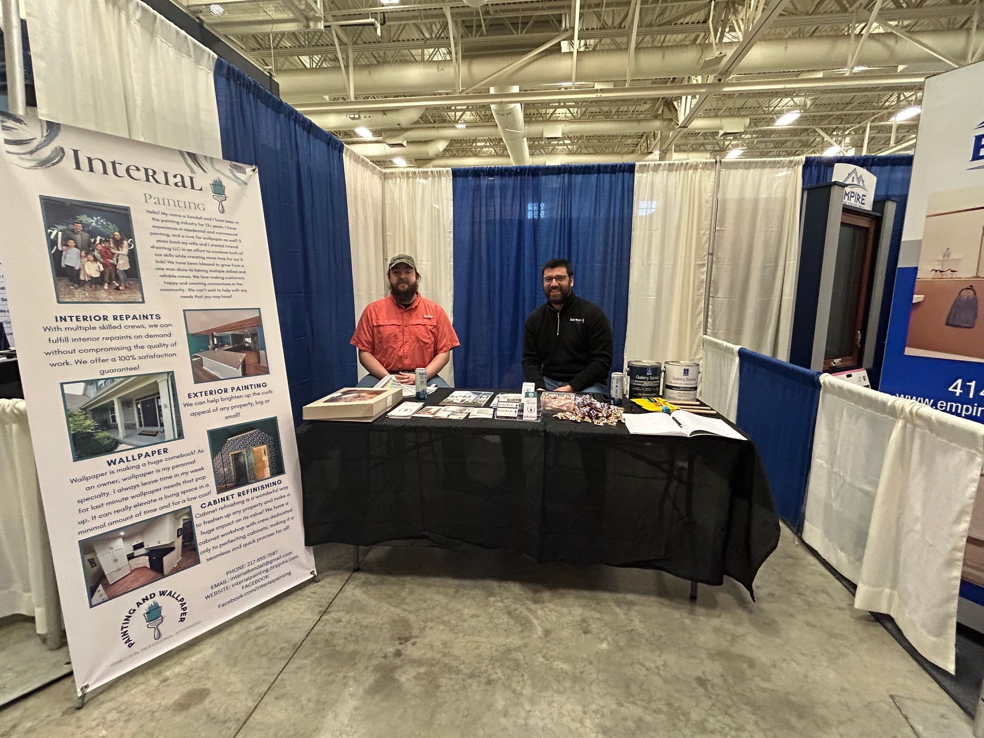 Two men are standing behind a table at a trade show.