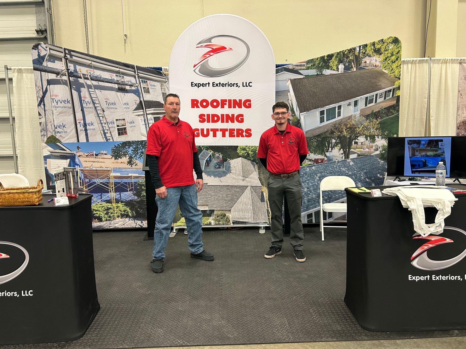 Two men are standing in front of a roofing siding booth.