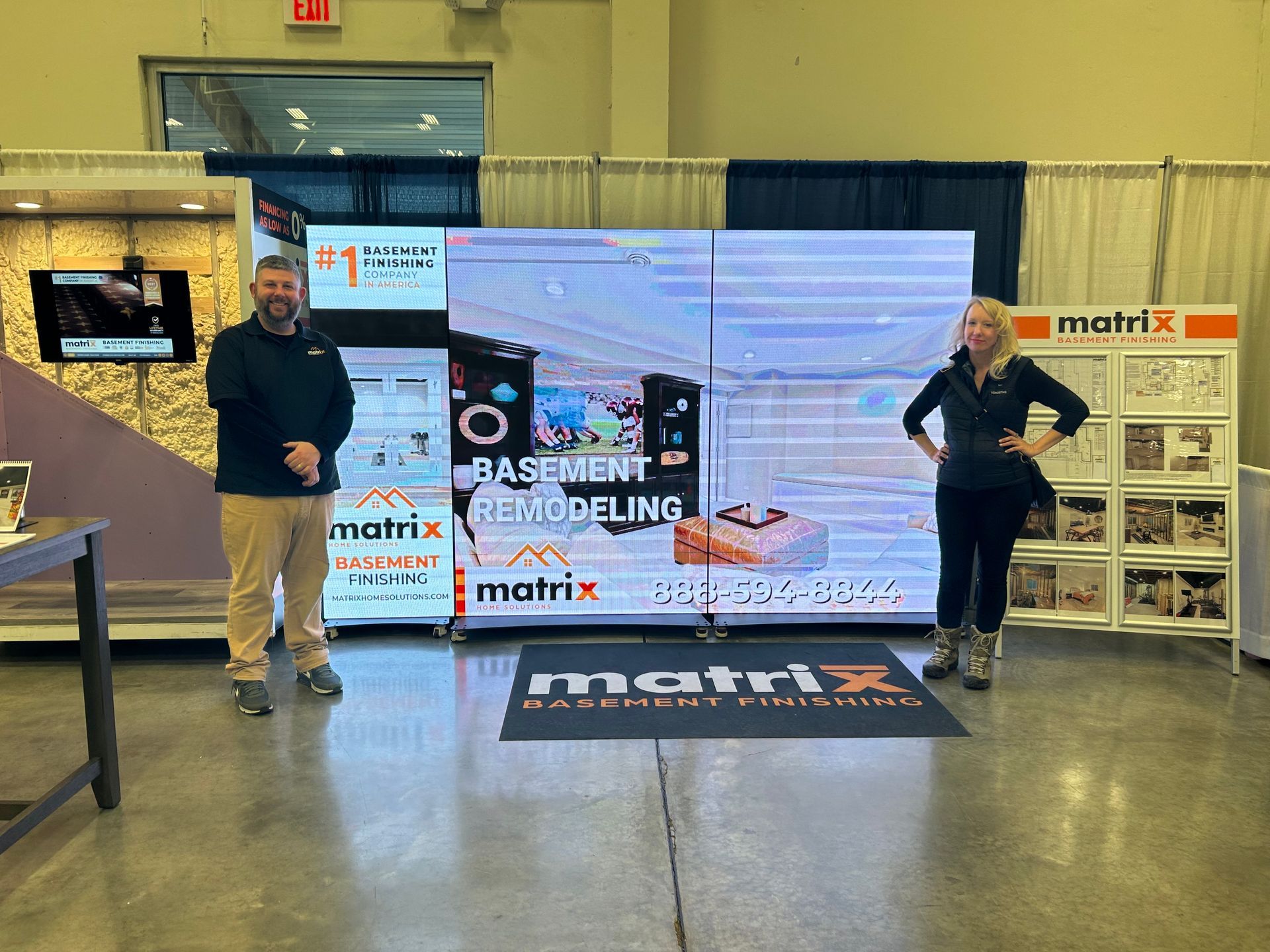 A man and a woman are standing in front of a large screen that says basement remodeling.