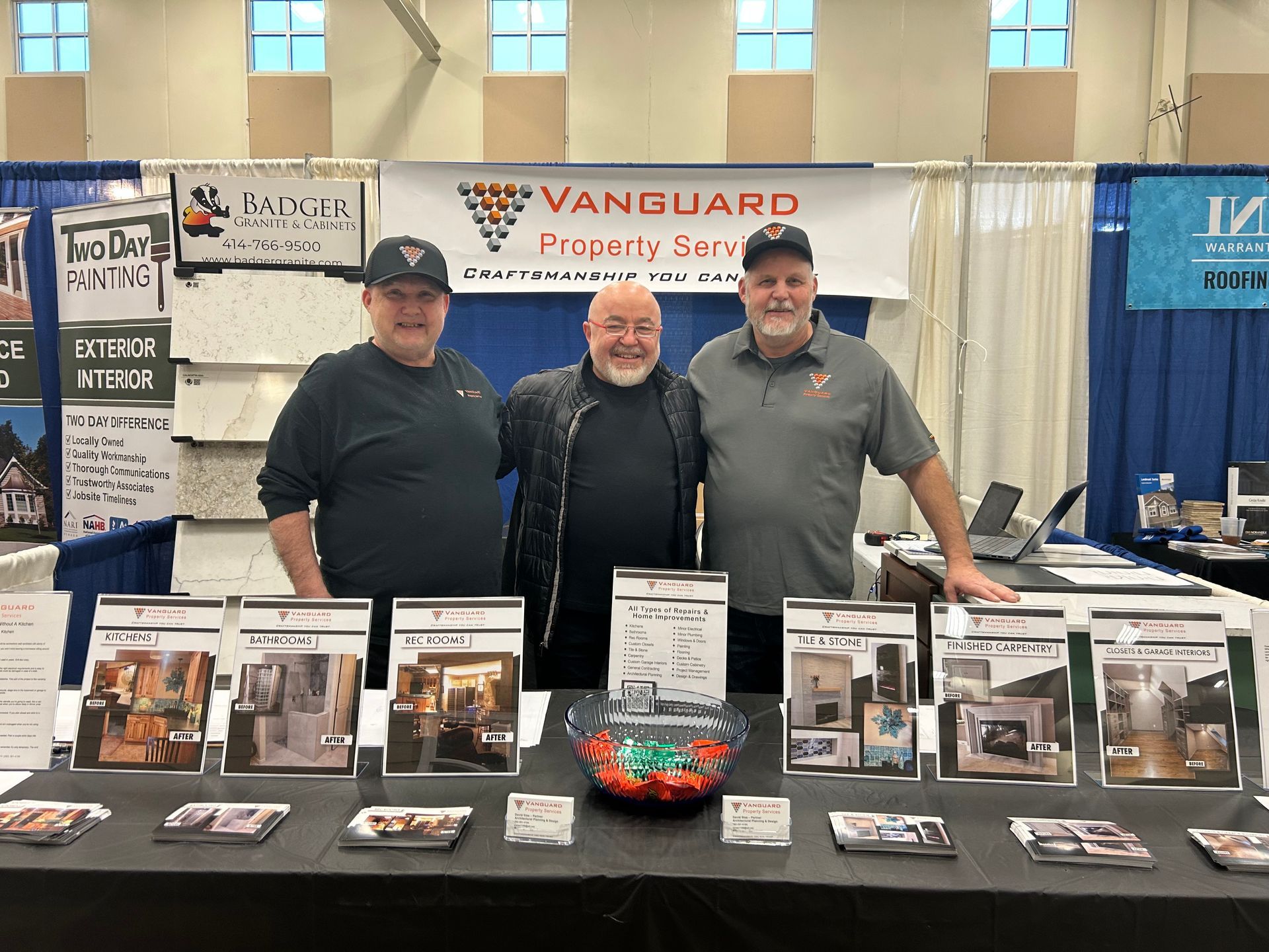 Three men are posing for a picture in front of a table with brochures on it.