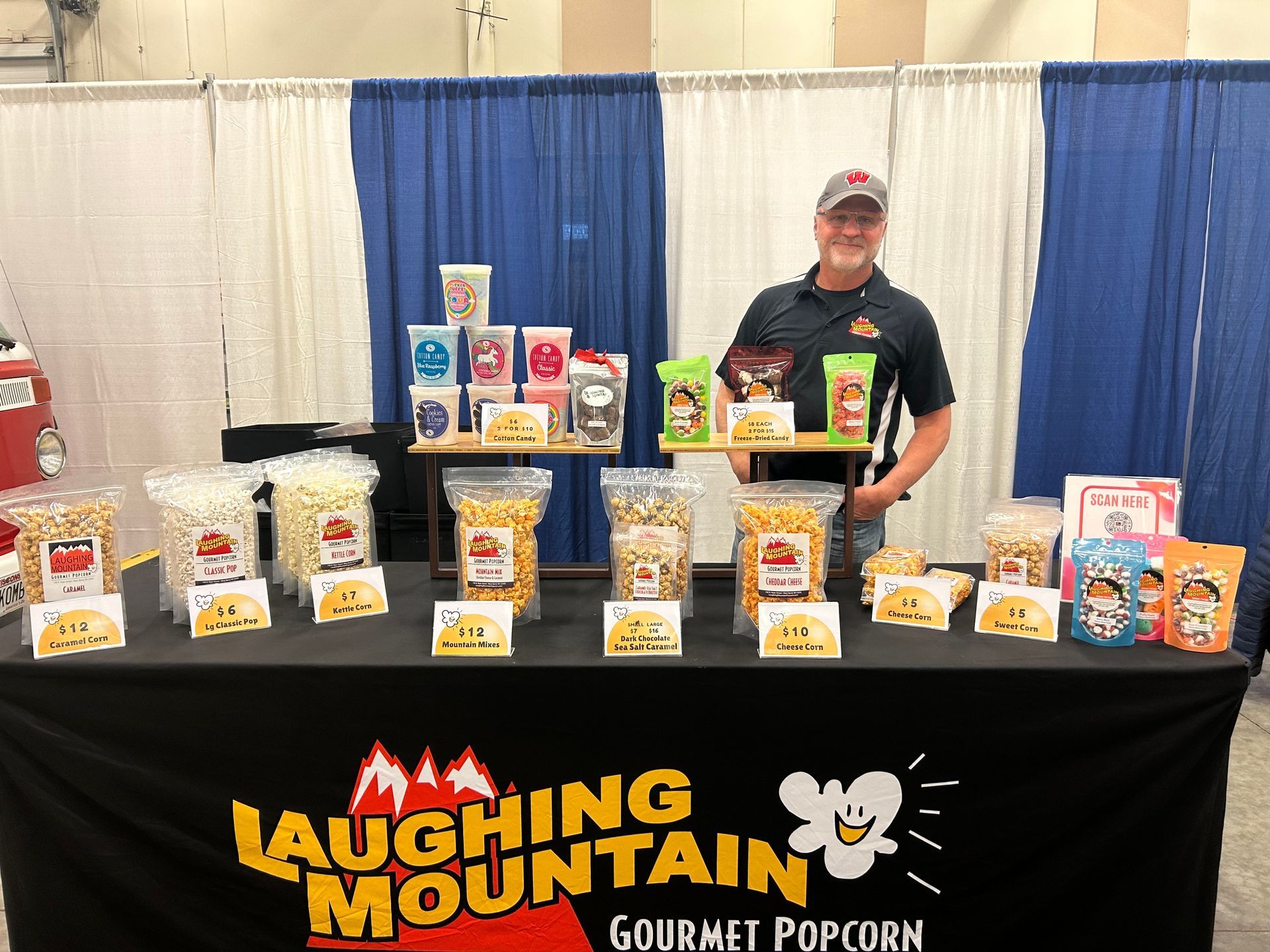 A man is standing in front of a table filled with bags of popcorn.