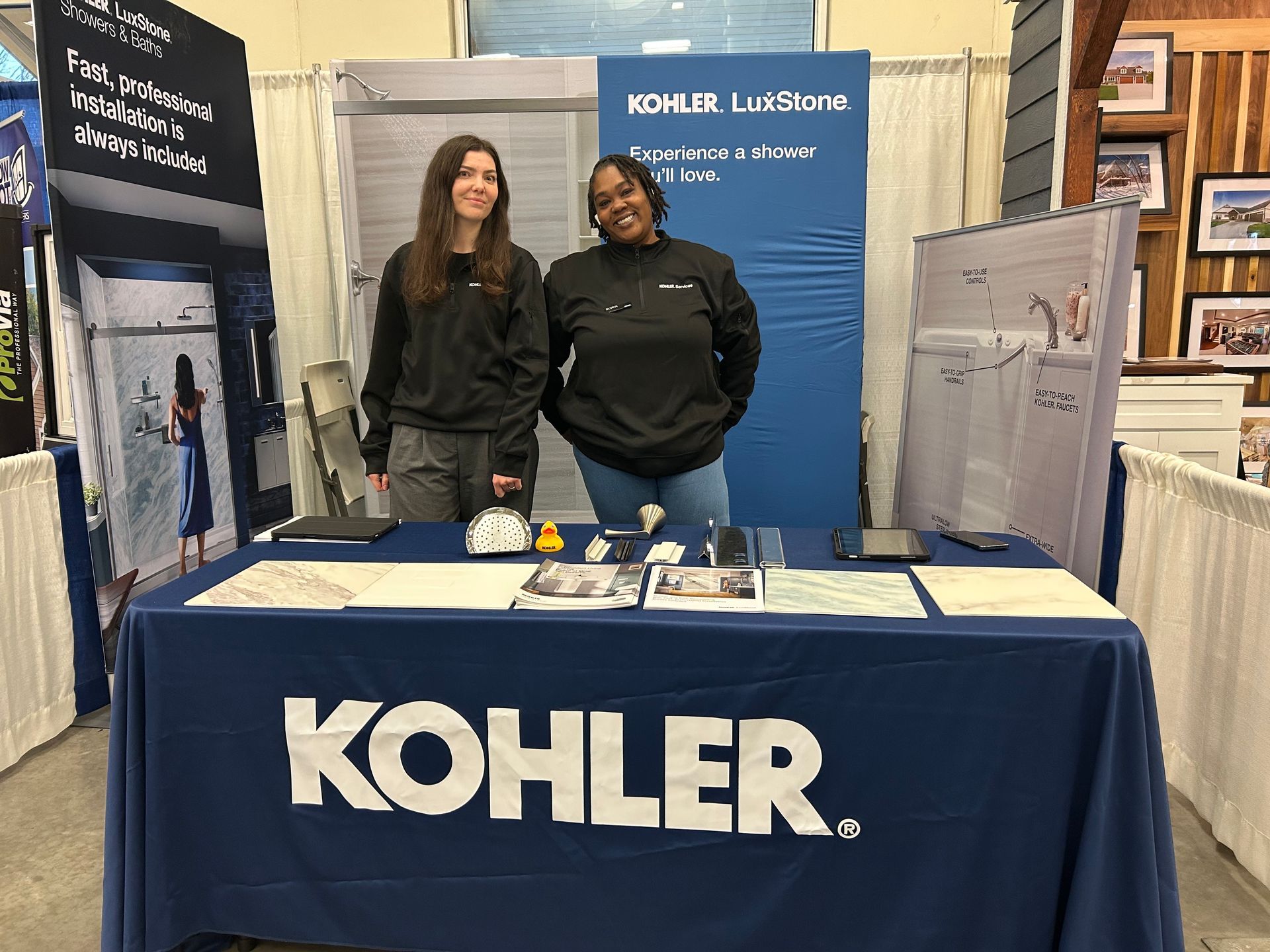 Two women are standing behind a kohler table.