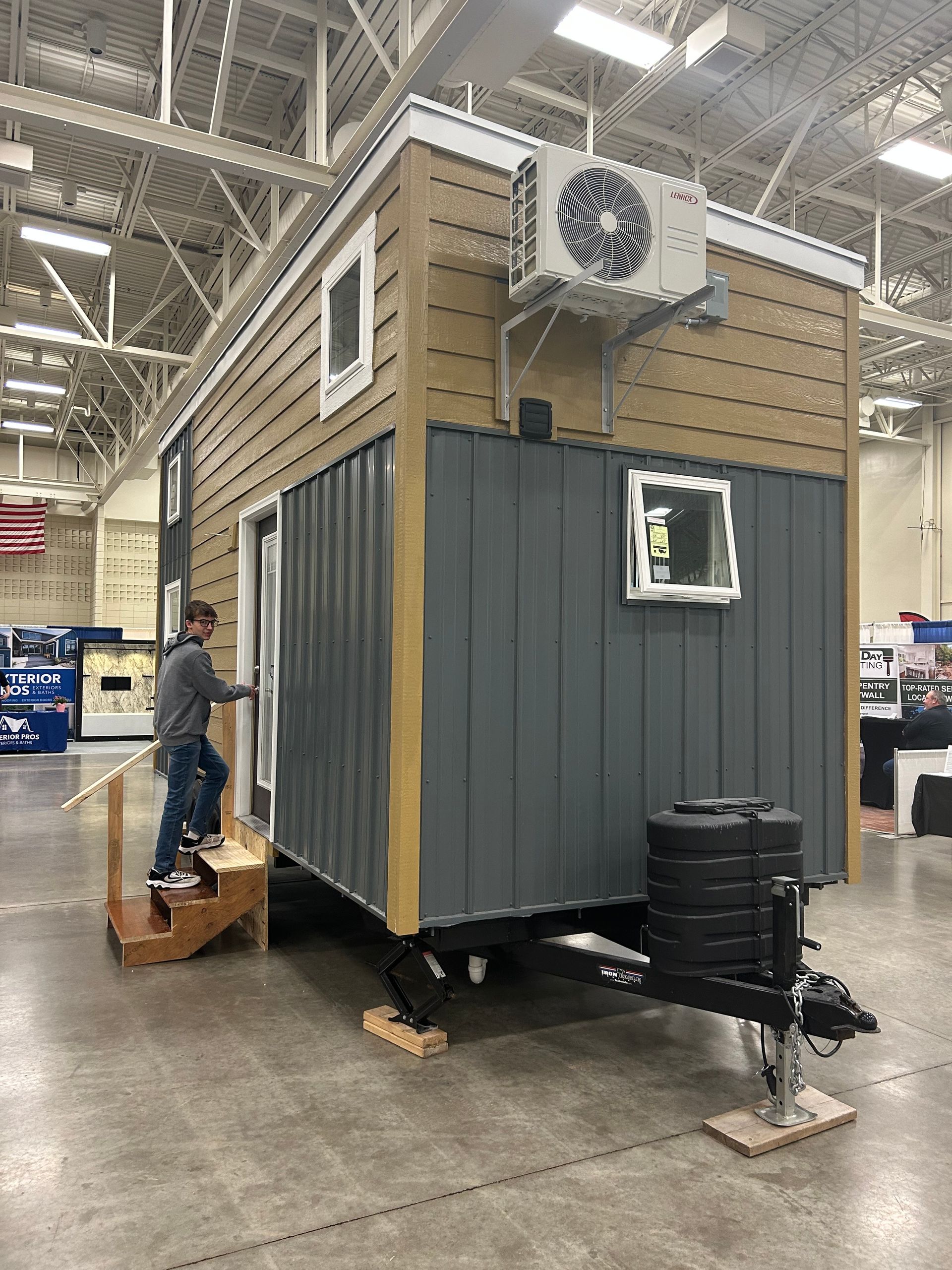 A man is standing in front of a tiny house on a trailer.