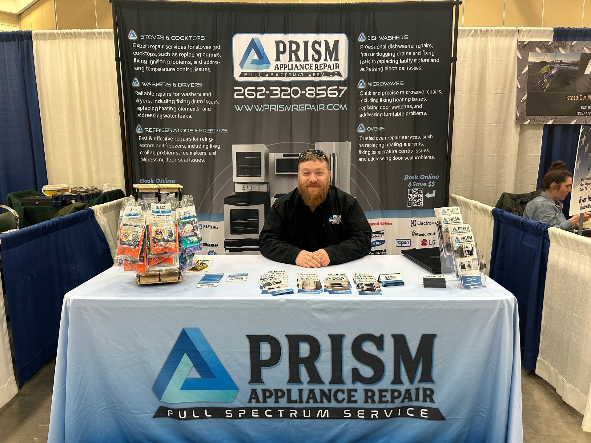 A man is sitting at a table in front of a sign that says prism appliance repair.