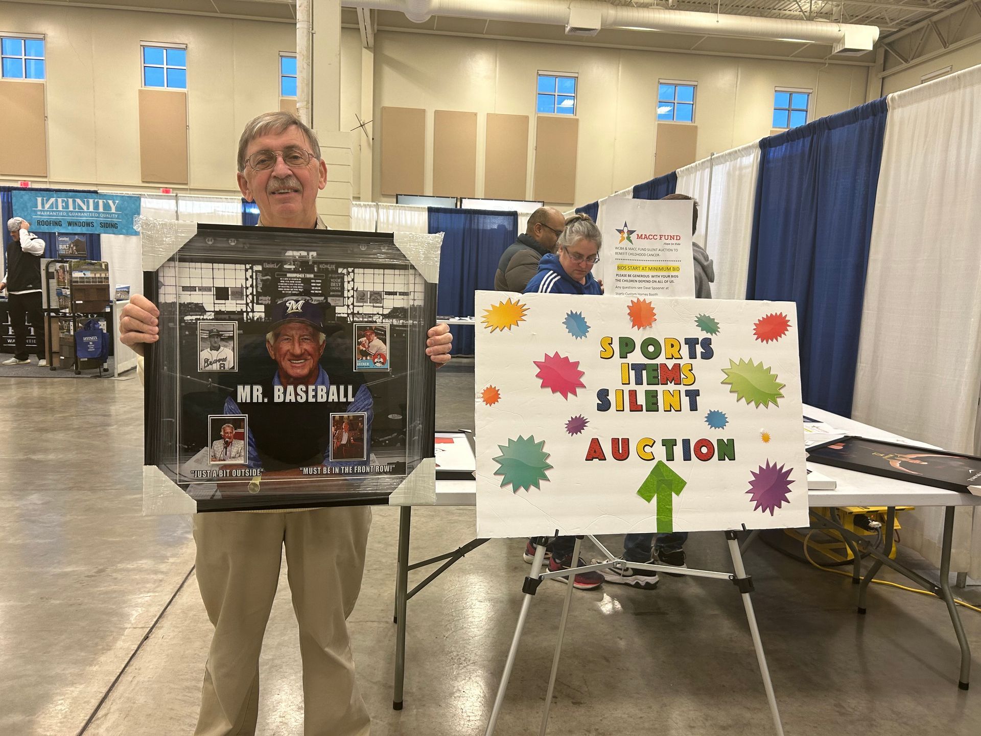 A man is holding a framed picture in front of a sports memorabilia auction sign.
