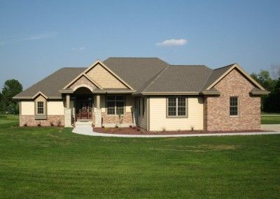 A large house with a brown roof sits in the middle of a lush green field