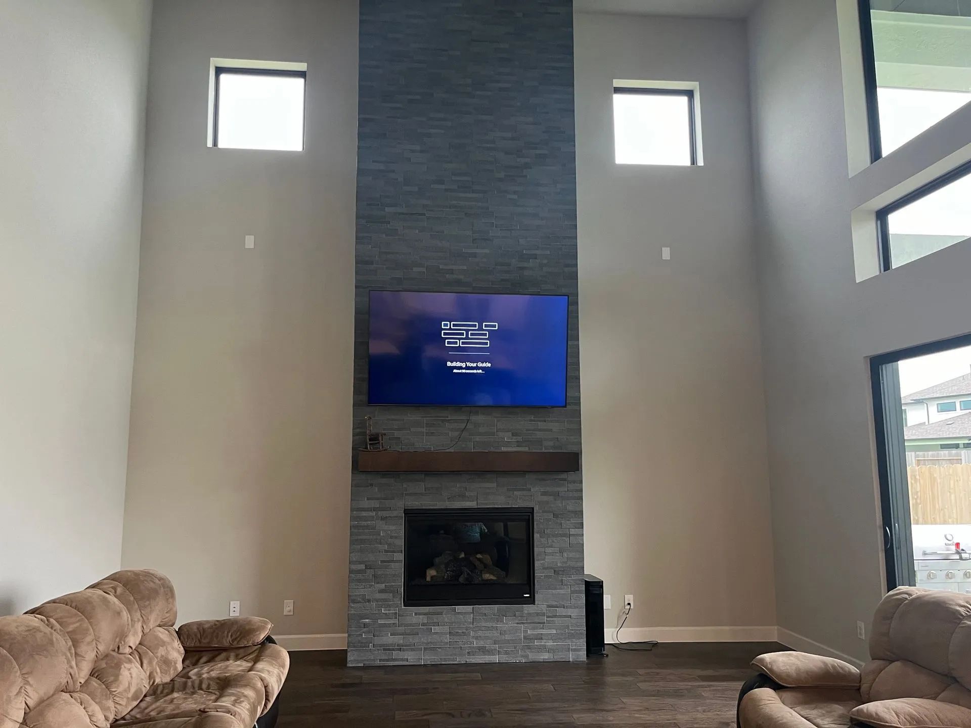 Living room with tall fireplace, mounted TV, beige sofa, and high windows