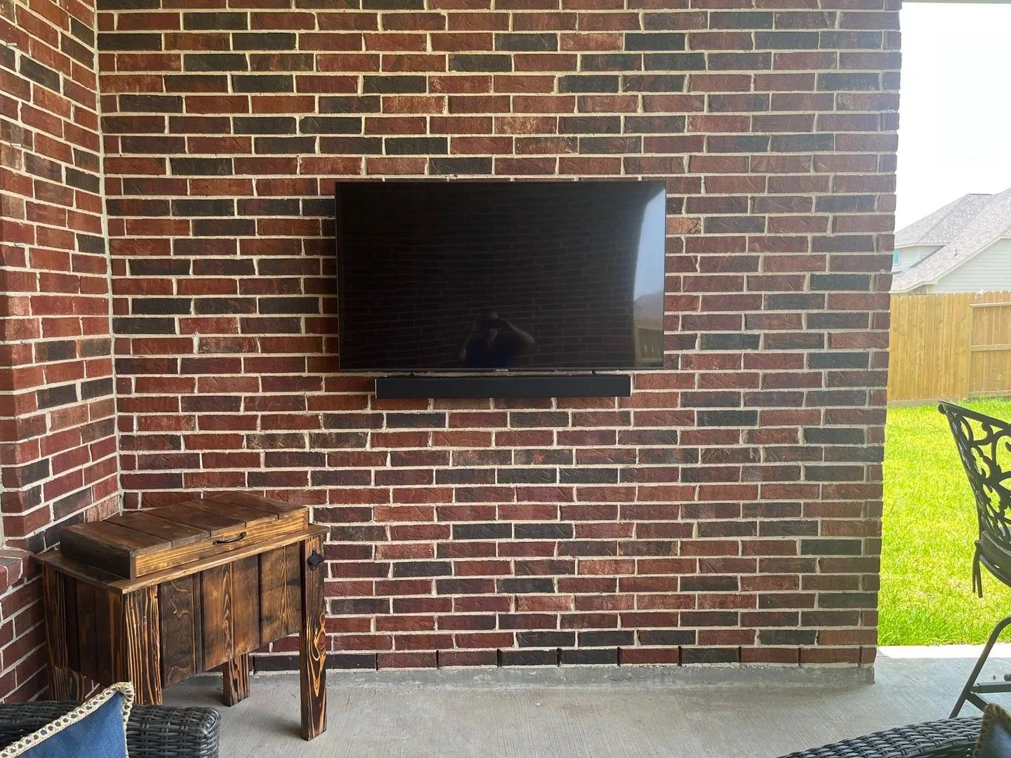 Brick wall with a wall-mounted TV and a small wooden table on a patio.