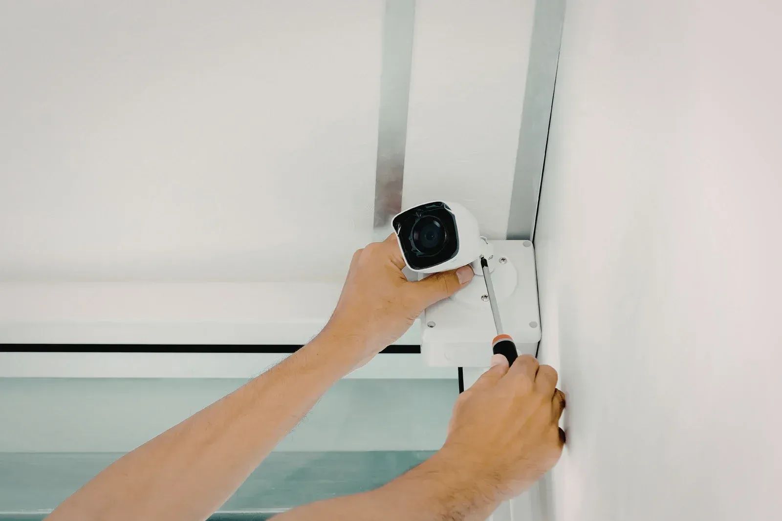 Hands mounting a white security camera near a ceiling corner.