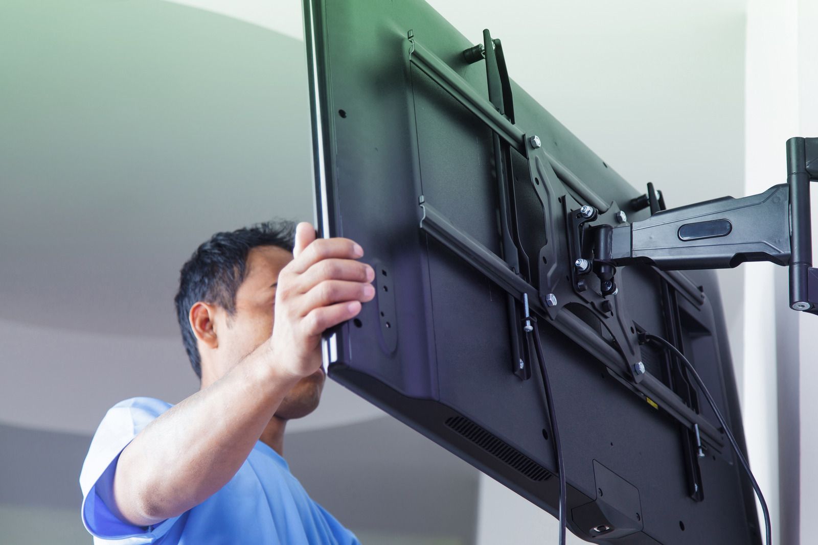 Person mounting a flat-screen TV on a wall bracket, adjusting it in a bright room