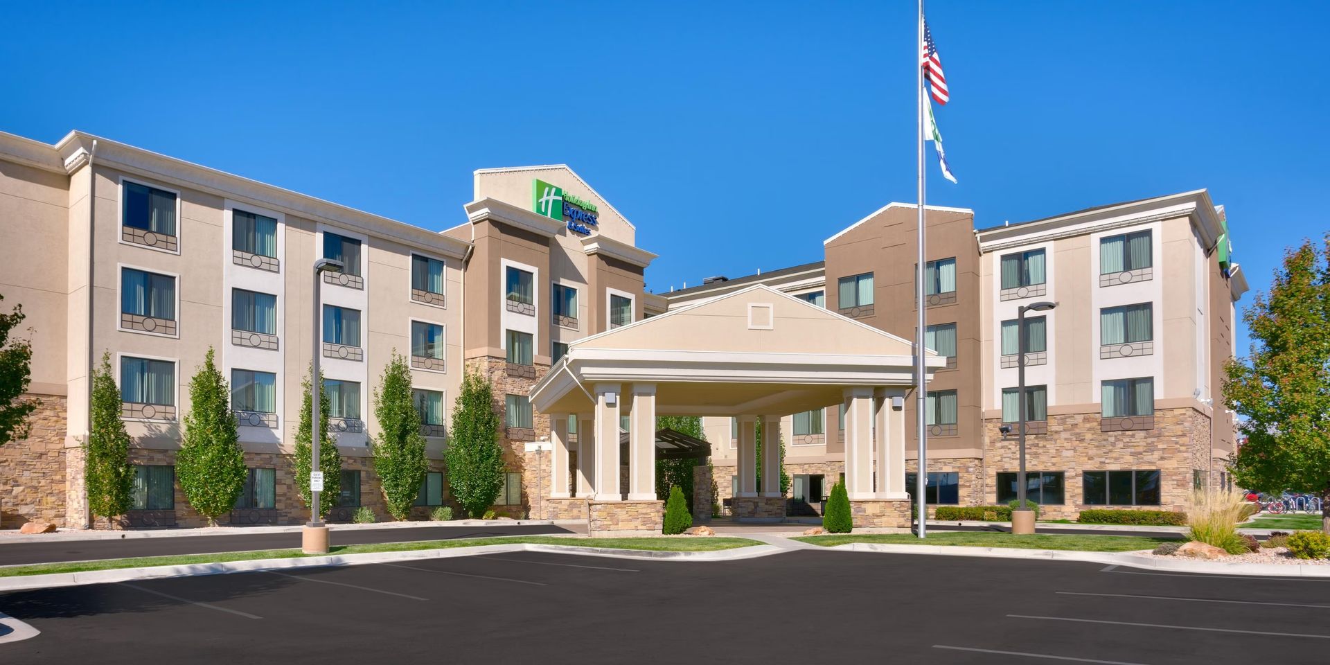 Hotel exterior with pool and lounge chairs. Blue sky overhead.