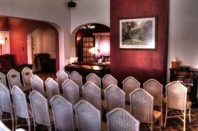 Rows of wicker chairs face a red wall with framed art in a room with arched doorways.