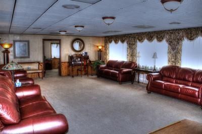 Room with red leather sofas, lamps, and a small piano. Beige carpet, floral curtains.