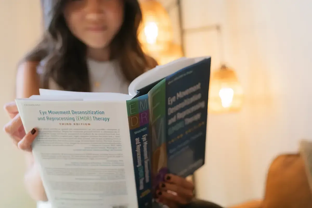 Person reading an open book indoors, with a second book held in the foreground