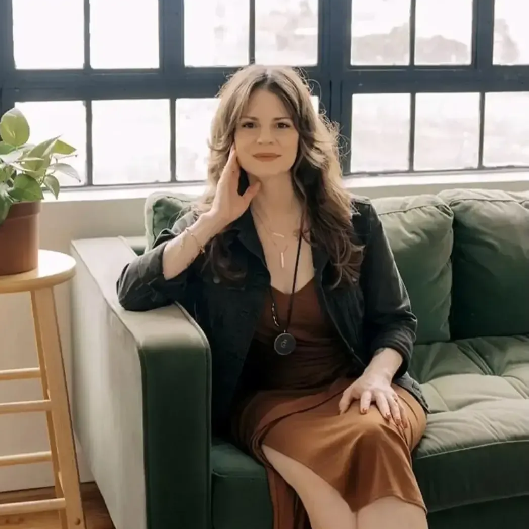 Woman seated on a green sofa in a bright living room by large windows